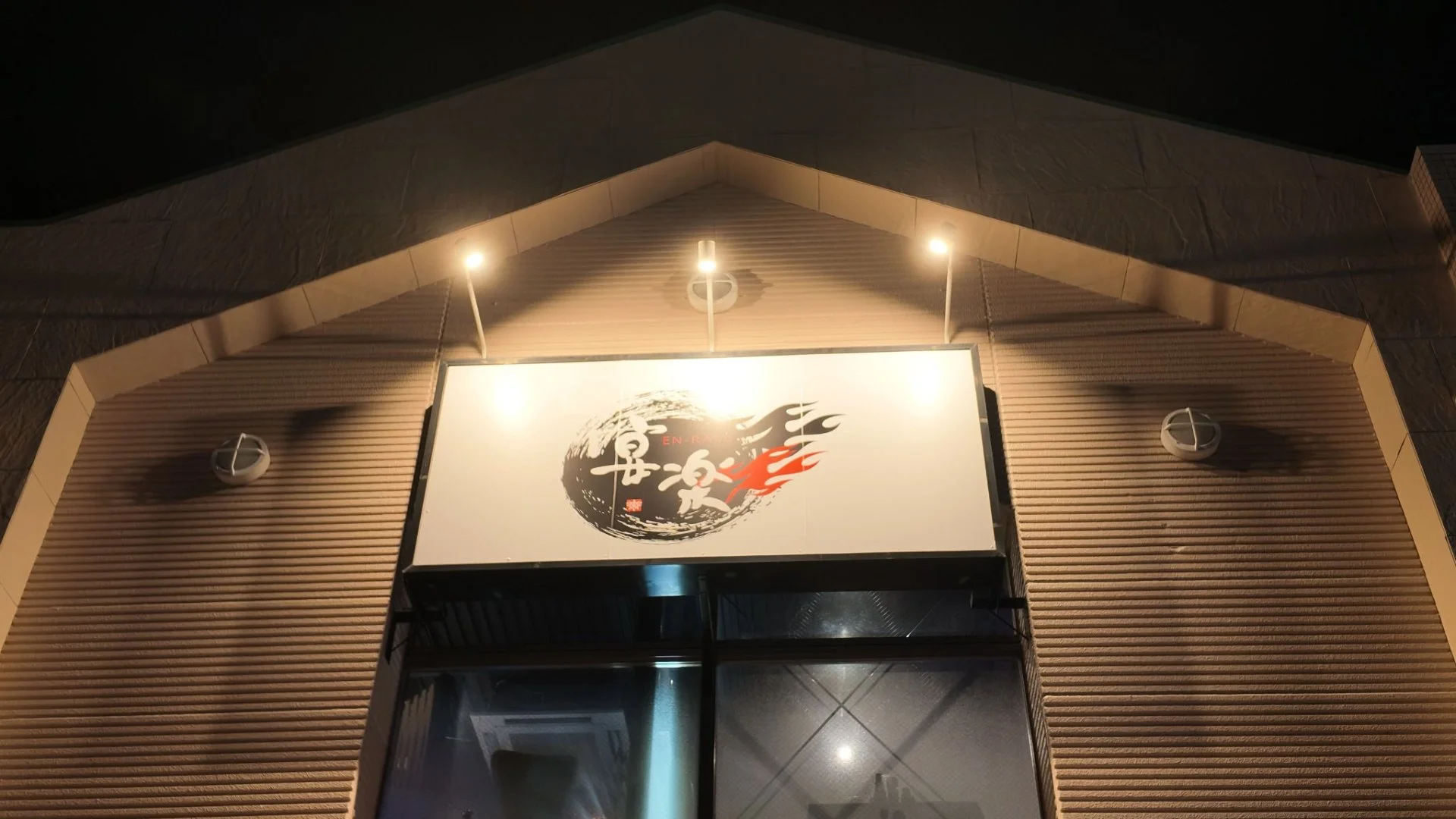 夜の暖色の照明に照らされた居酒屋 宴楽の看板と外観